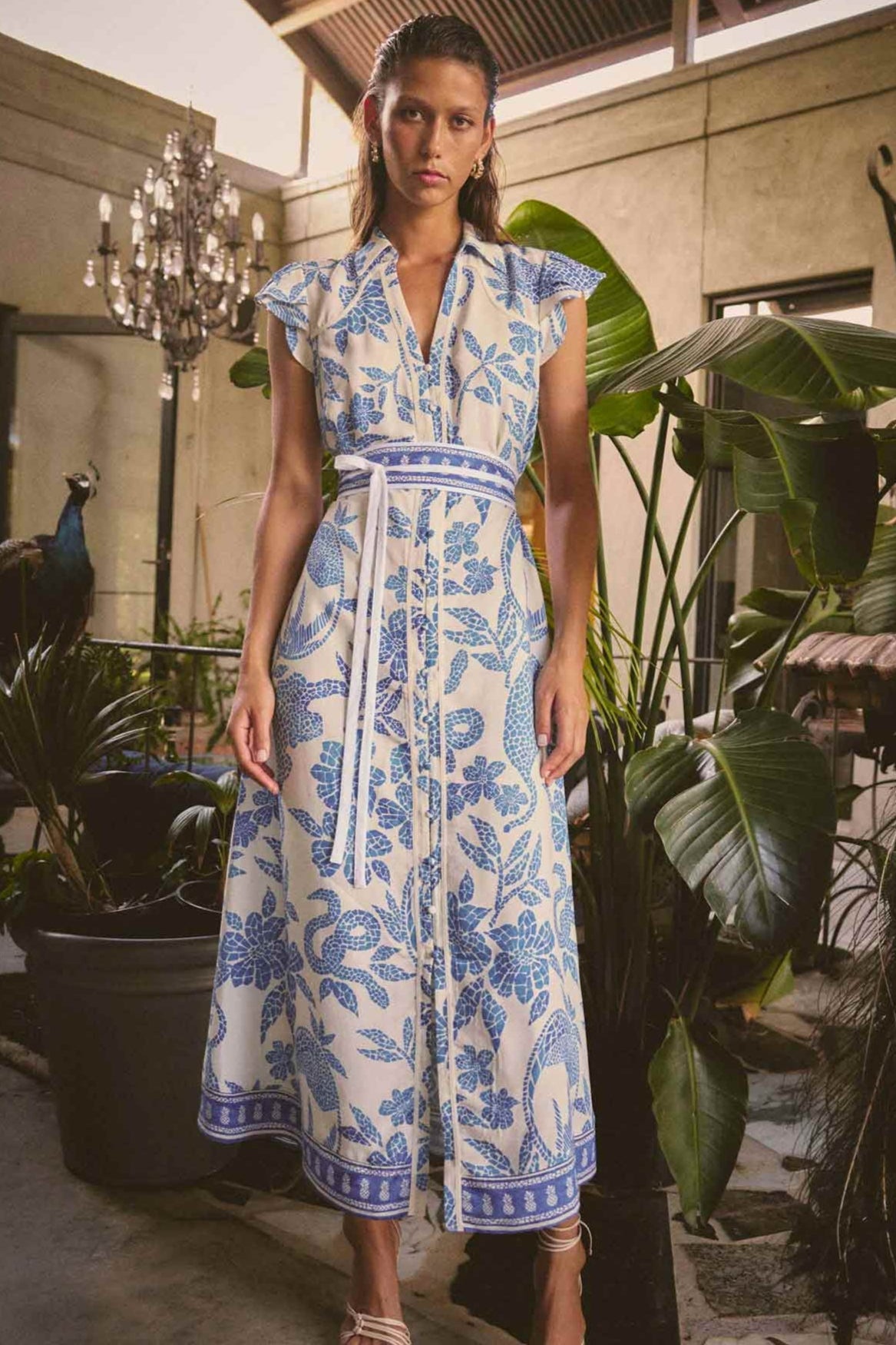 Woman in a blue and white floral dress standing in an indoor setting with plants.